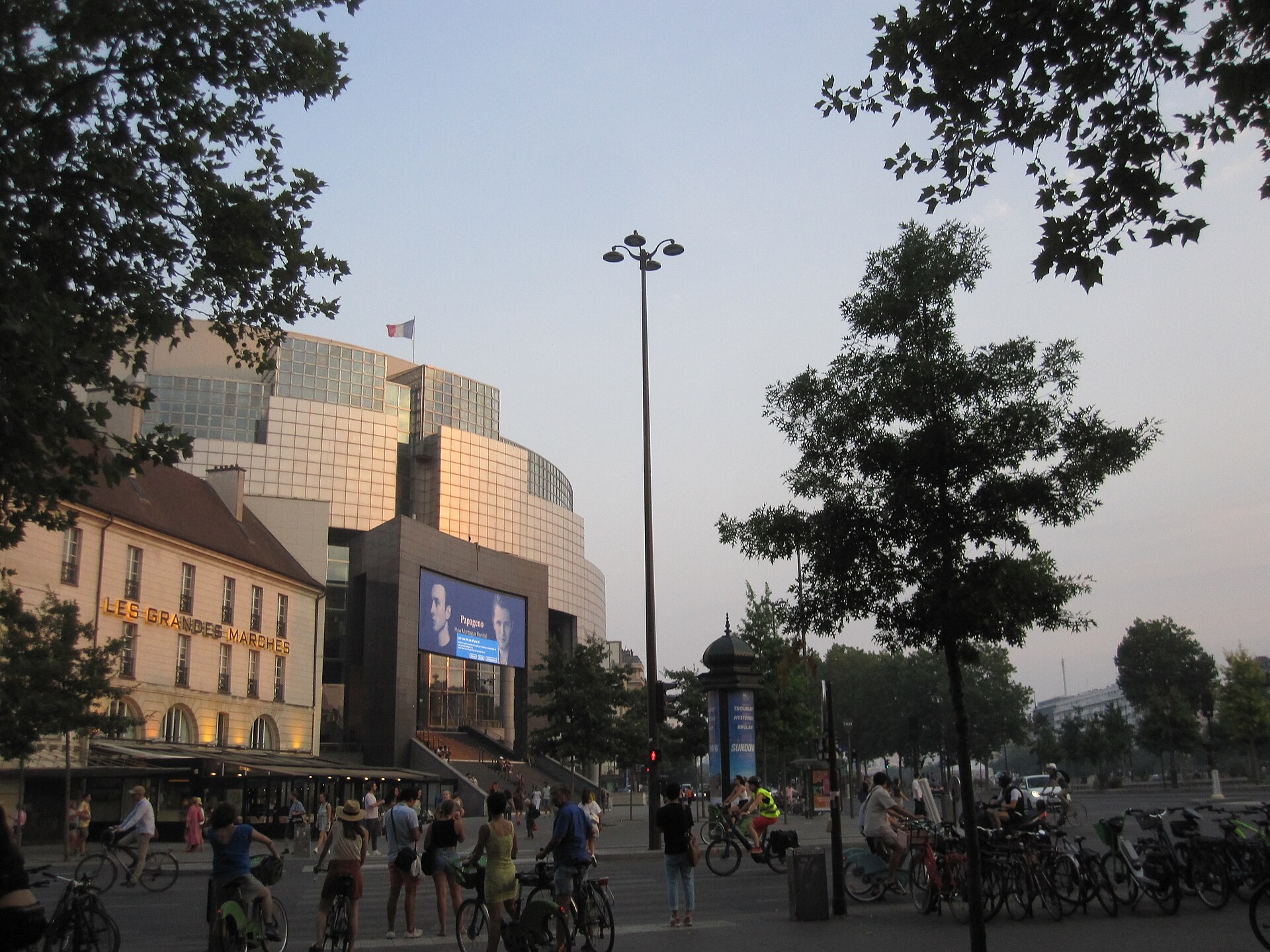 Opéra Bastille au crépuscule, façade de verre, restaurant Les Grandes Marches, écran, vélos place de la Bastille.